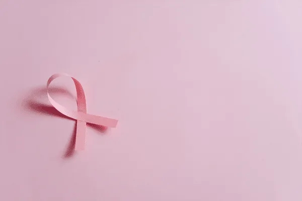 A pink awareness ribbon, symbolizing breast cancer awareness, is placed on a pink background with ample empty space to the right—reflecting MorningStar Senior Living Hillsboro’s commitment to wellness in retirement living.
