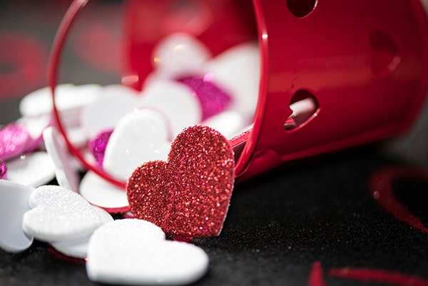 A small red bucket tipped over, spilling out sparkly red, white, and pink heart-shaped decorations onto a dark surface—capturing the warmth and joy found at MorningStar Senior Living Hillsboro.