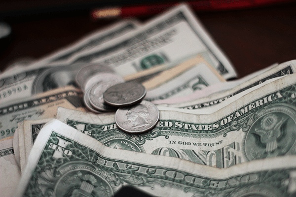 A close-up of several U.S. dollar bills and coins scattered on a flat surface, reflecting budgeting and financial planning often considered in Retirement Living at MorningStar Senior Living Hillsboro. Various denominations and a few quarters are visible among the cash.
