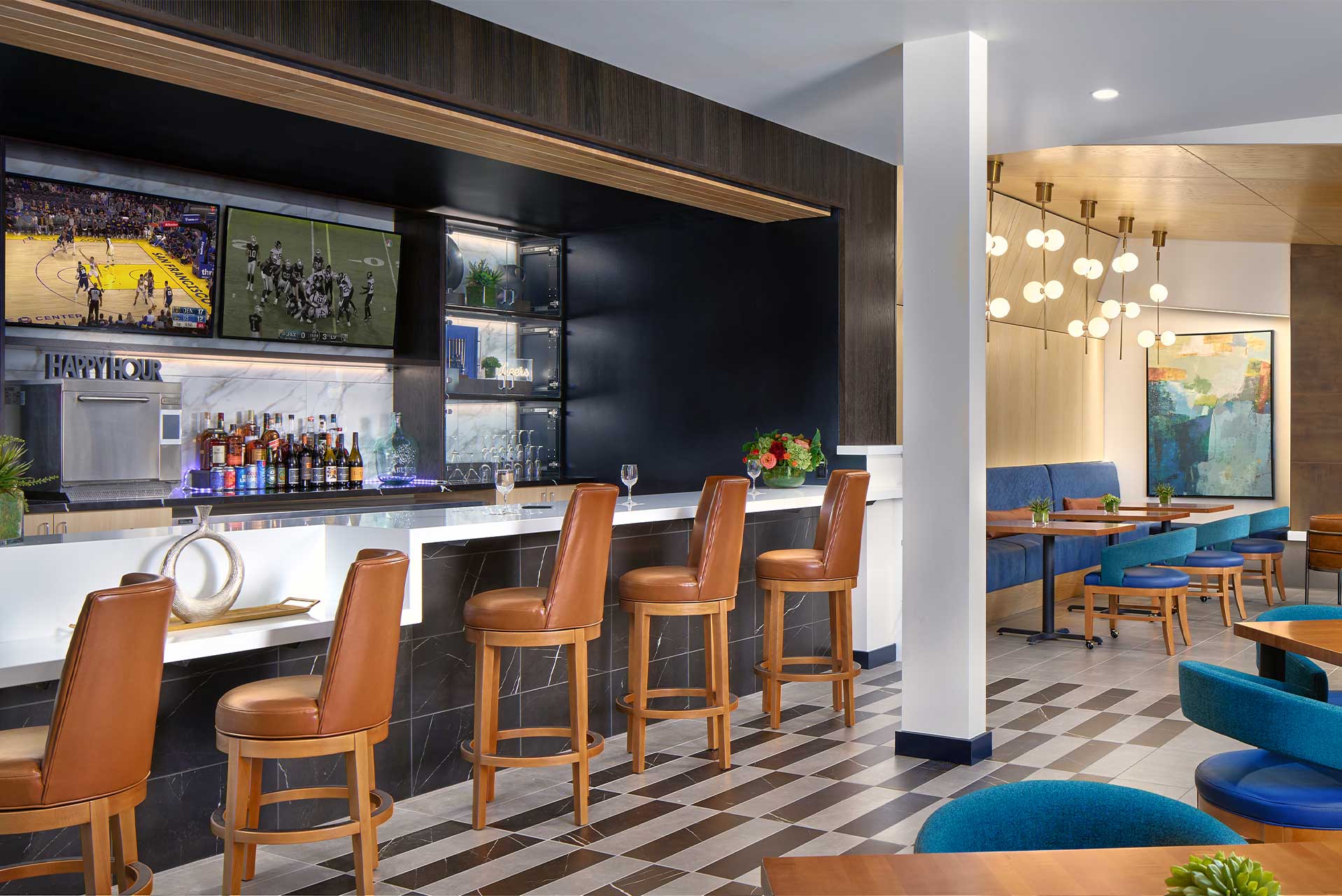 Modern hotel bar with brown leather barstools, a well-stocked counter, two TVs showing sports, and contemporary lighting—ideal for gatherings at MorningStar Senior Living Hillsboro or those seeking stylish retirement living.