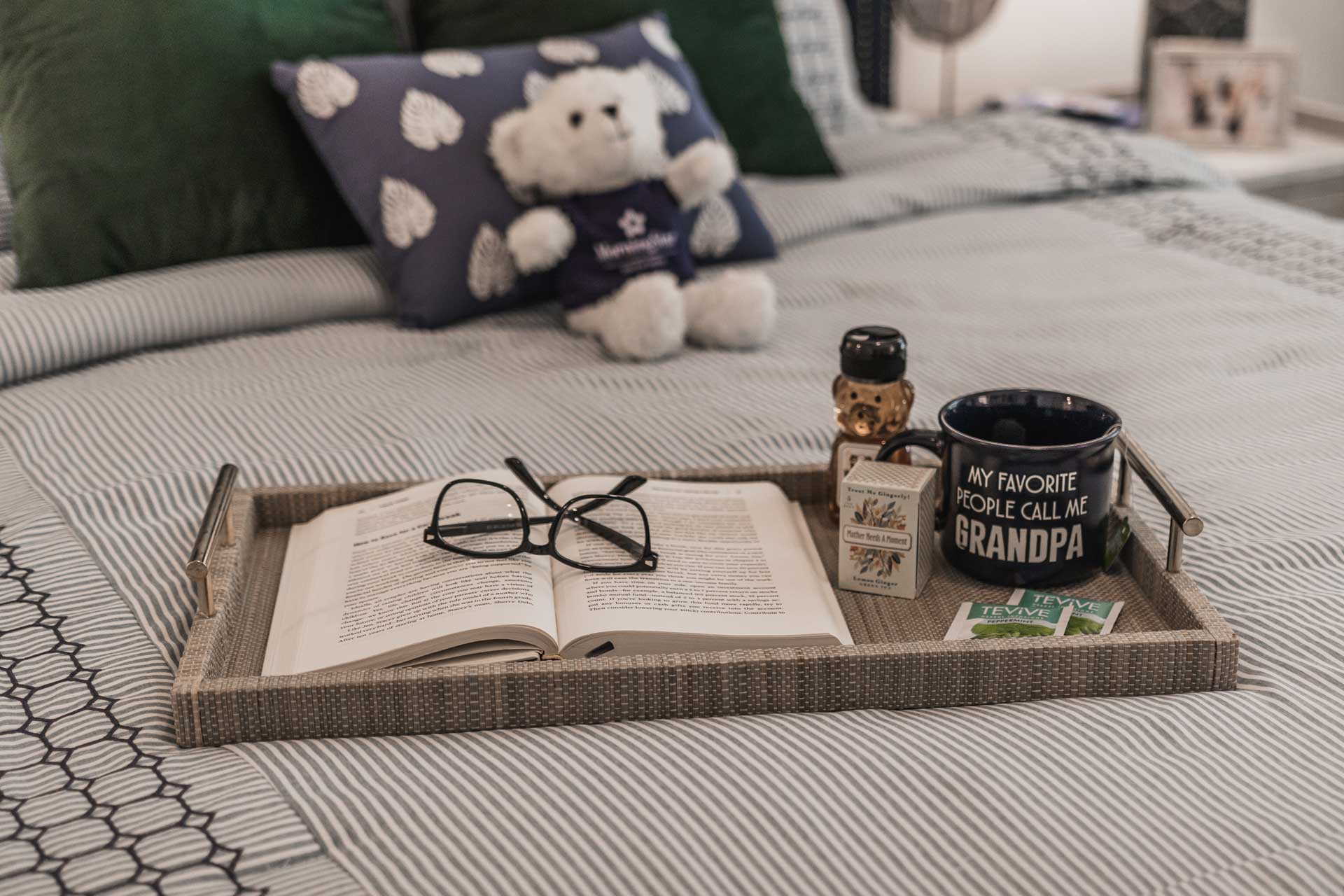 A tray on a striped bed at MorningStar Senior Living Hillsboro holds an open book, glasses, a 
