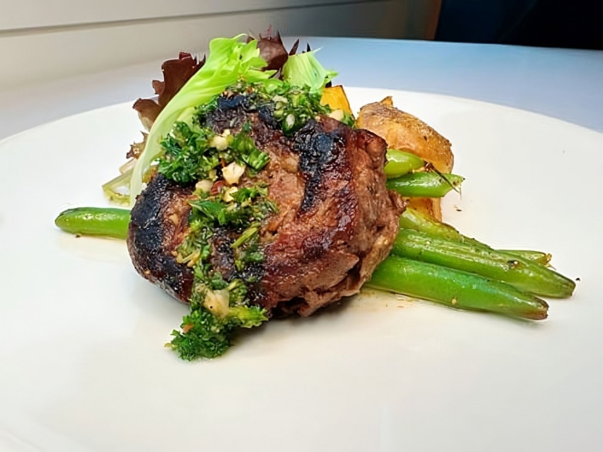 A delicious grilled steak topped with chopped herbs sits on green beans, with roasted potatoes and mixed greens—a delightful meal enjoyed at MorningStar Senior Living Hillsboro, where retirement living means savoring every bite.