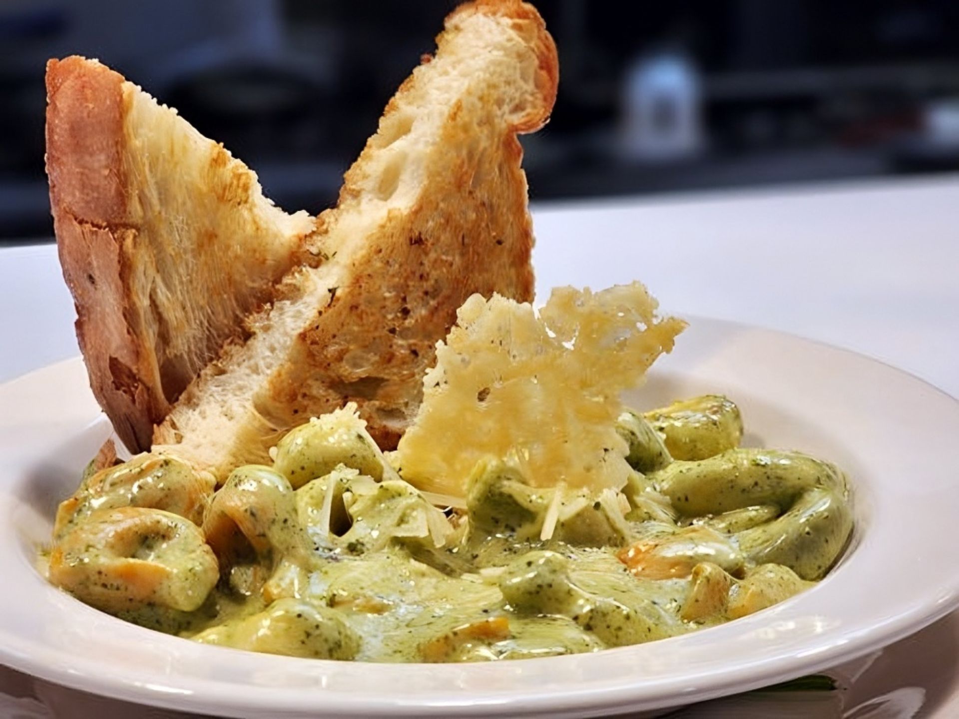A bowl of tortellini in creamy green pesto sauce, topped with shredded cheese and a crisp cheese garnish, served with two slices of toasted bread—just one of the delicious meals enjoyed at MorningStar Senior Living Hillsboro Retirement Living.