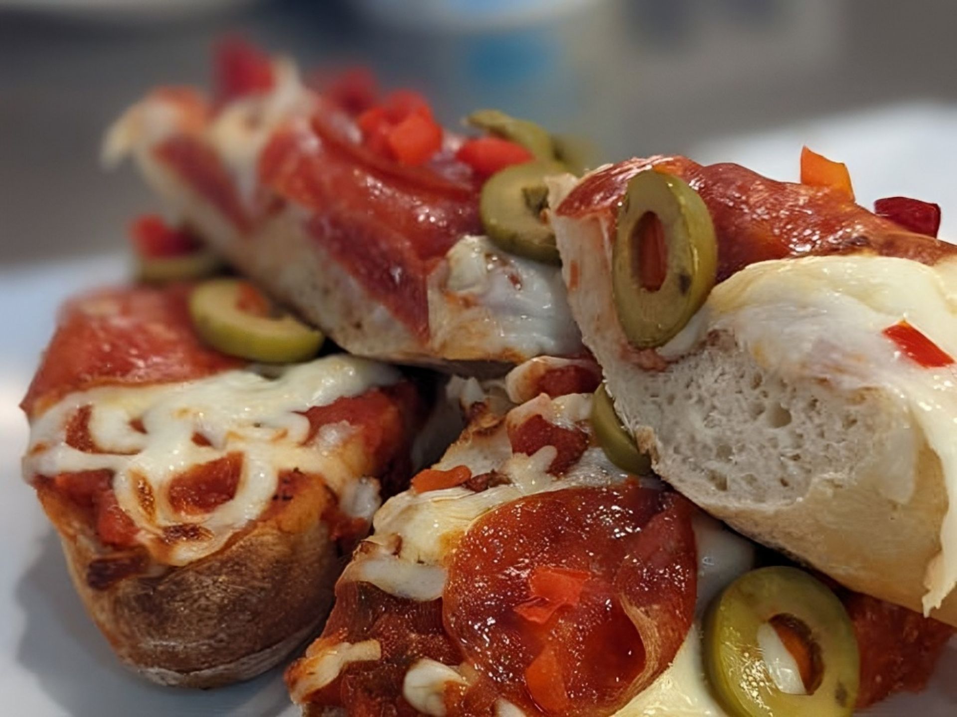 Close-up of pizza bread slices topped with melted cheese, pepperoni, green olives, and diced red peppers, stacked on a white plate—a delicious taste of Retirement Living at MorningStar Senior Living Hillsboro. The crust appears thick and slightly browned.
