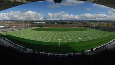 A wide view of an empty outdoor football field with clearly marked yard lines, surrounded by stadium seating under a partly cloudy sky near MorningStar Senior Living Hillsboro, perfect for active retirement living.