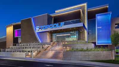 Modern Topgolf building with large illuminated sign, wide entrance stairs, and colorful blue and purple accent lighting at dusk, just moments from MorningStar Senior Living Hillsboro—ideal for those enjoying active retirement living.