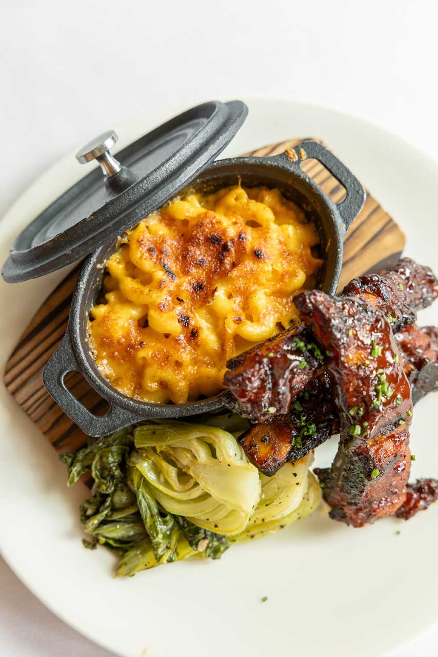 A plate with baked macaroni and cheese in a mini cast-iron pot, glazed ribs stacked on the side, and sautéed greens—all beautifully presented at MorningStar Senior Living Hillsboro for elevated retirement living.