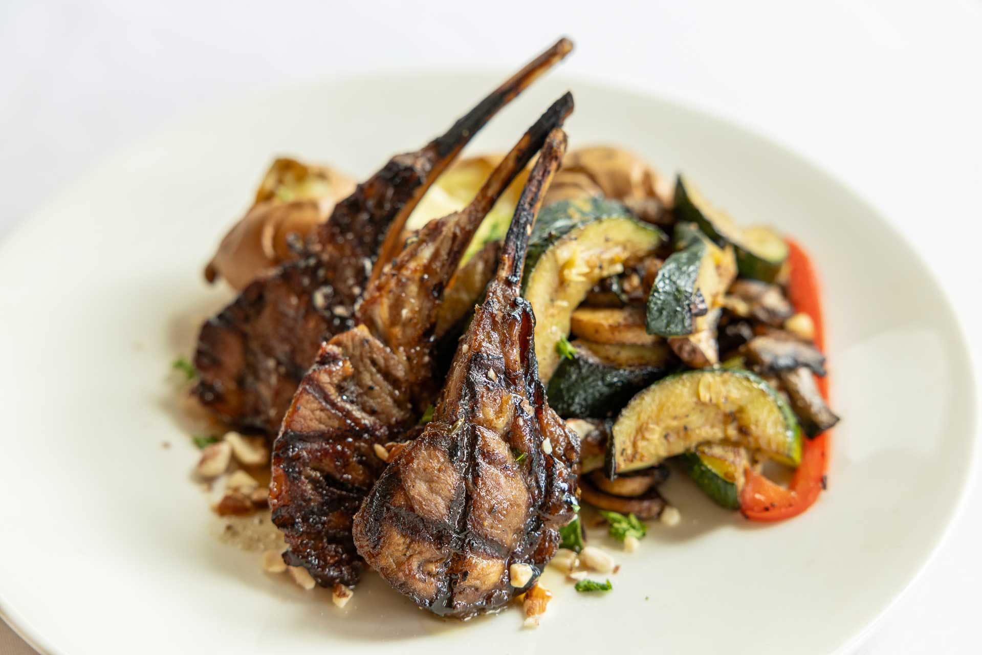 Grilled lamb chops served with a side of sautéed vegetables, including zucchini, mushrooms, and red peppers, on a white plate—a delicious option at MorningStar Senior Living Hillsboro for exceptional retirement living.