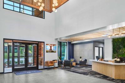 A modern, spacious lobby at MorningStar Senior Living Hillsboro features large windows, contemporary furniture, a reception desk, indoor plants, and hanging lights. Natural light fills the area, creating a welcoming Retirement Living atmosphere.