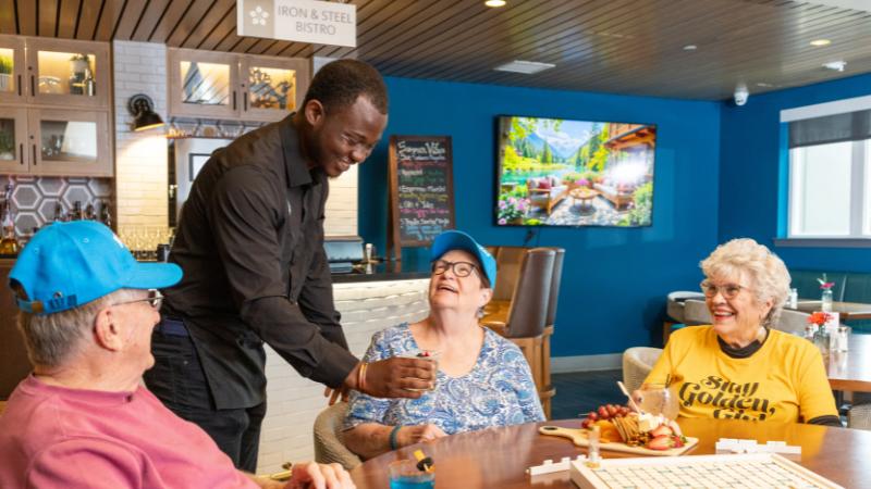 A group of seniors playing scrabble, being served drinks