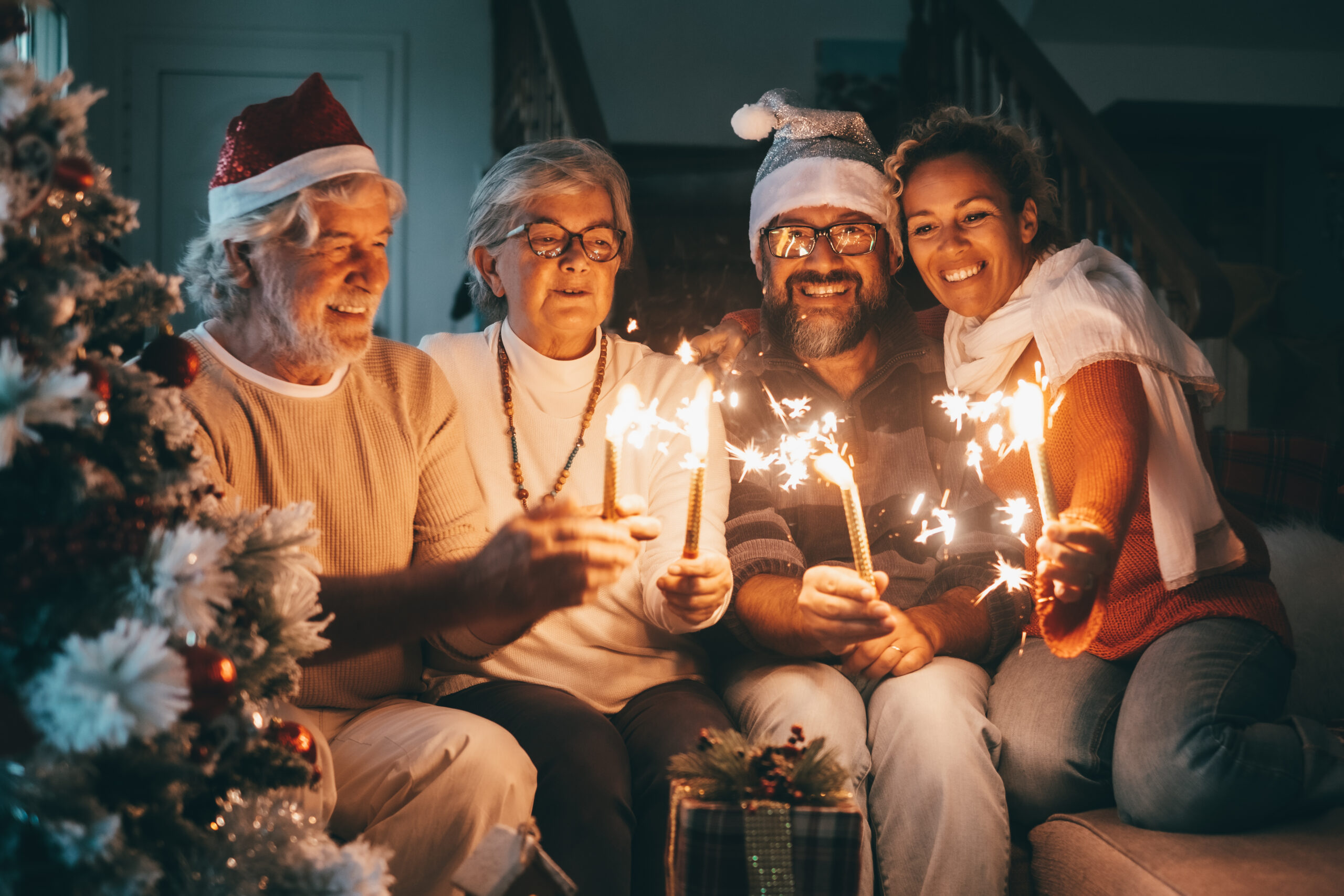 A smiling group of seniors holding sparklers and wearing Santa hats